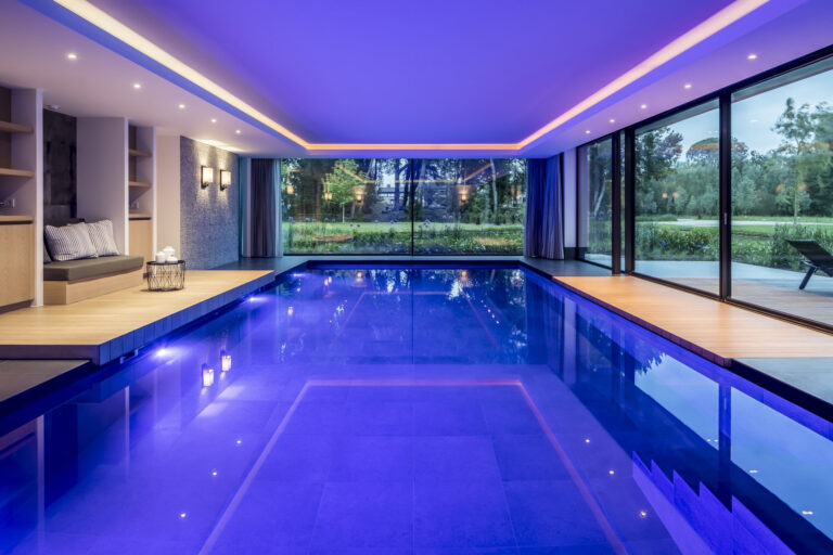 Binnenzwembad met blauwe sfeerverlichting en glazen wand